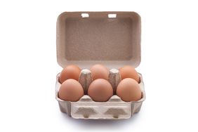 Close-Up Of Brown Eggs In Carton Over White Background