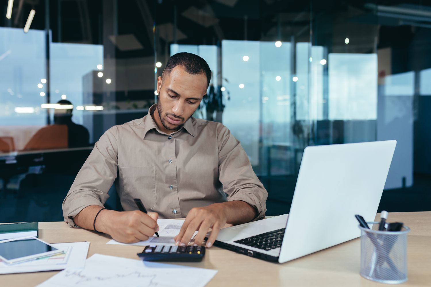 Loan officer at work grading loans for approval process using documents, calculator and laptop.