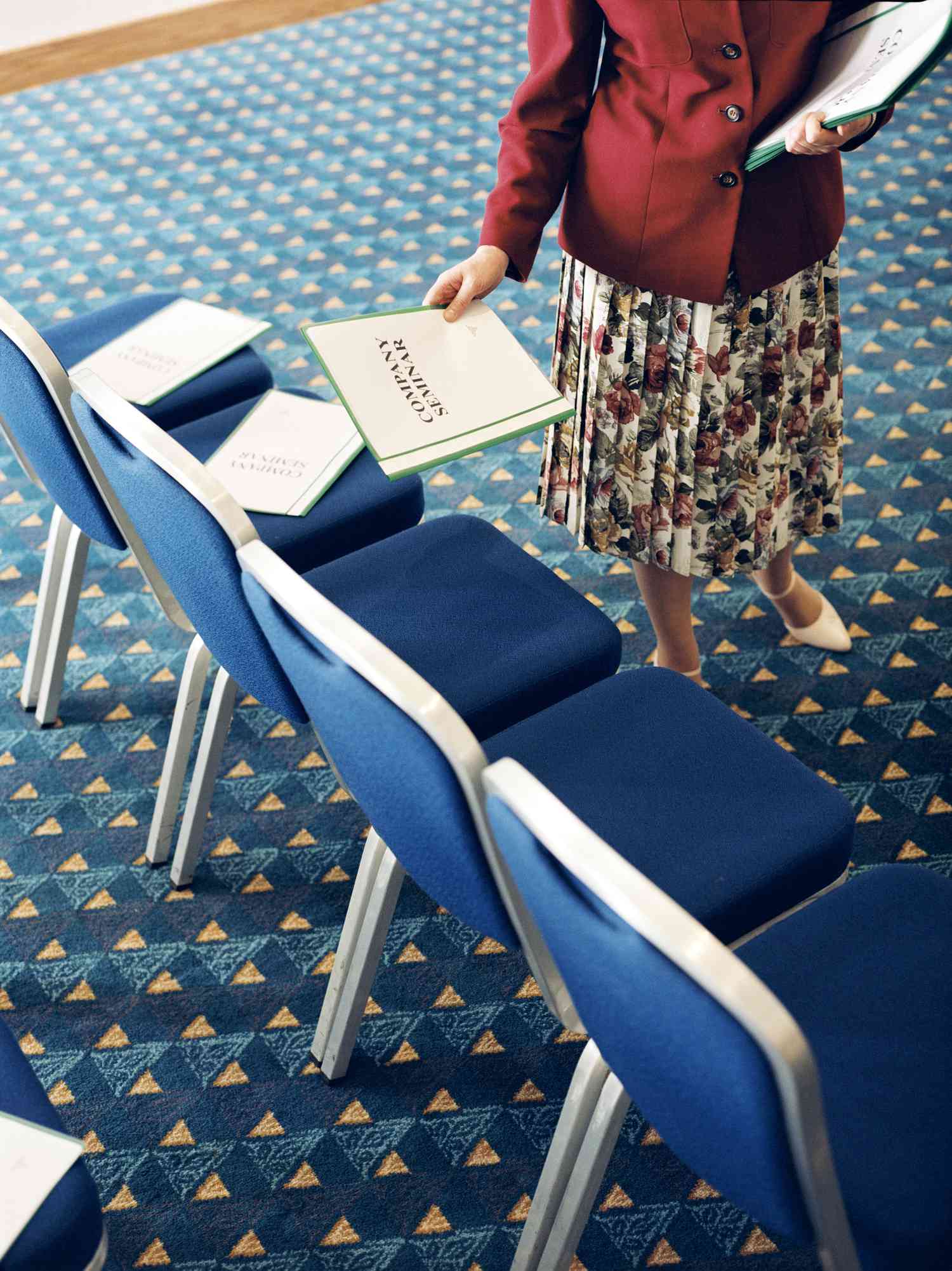 An employee places company summary reports onto the seats of chairs in a conference space in preparation for a meeting.