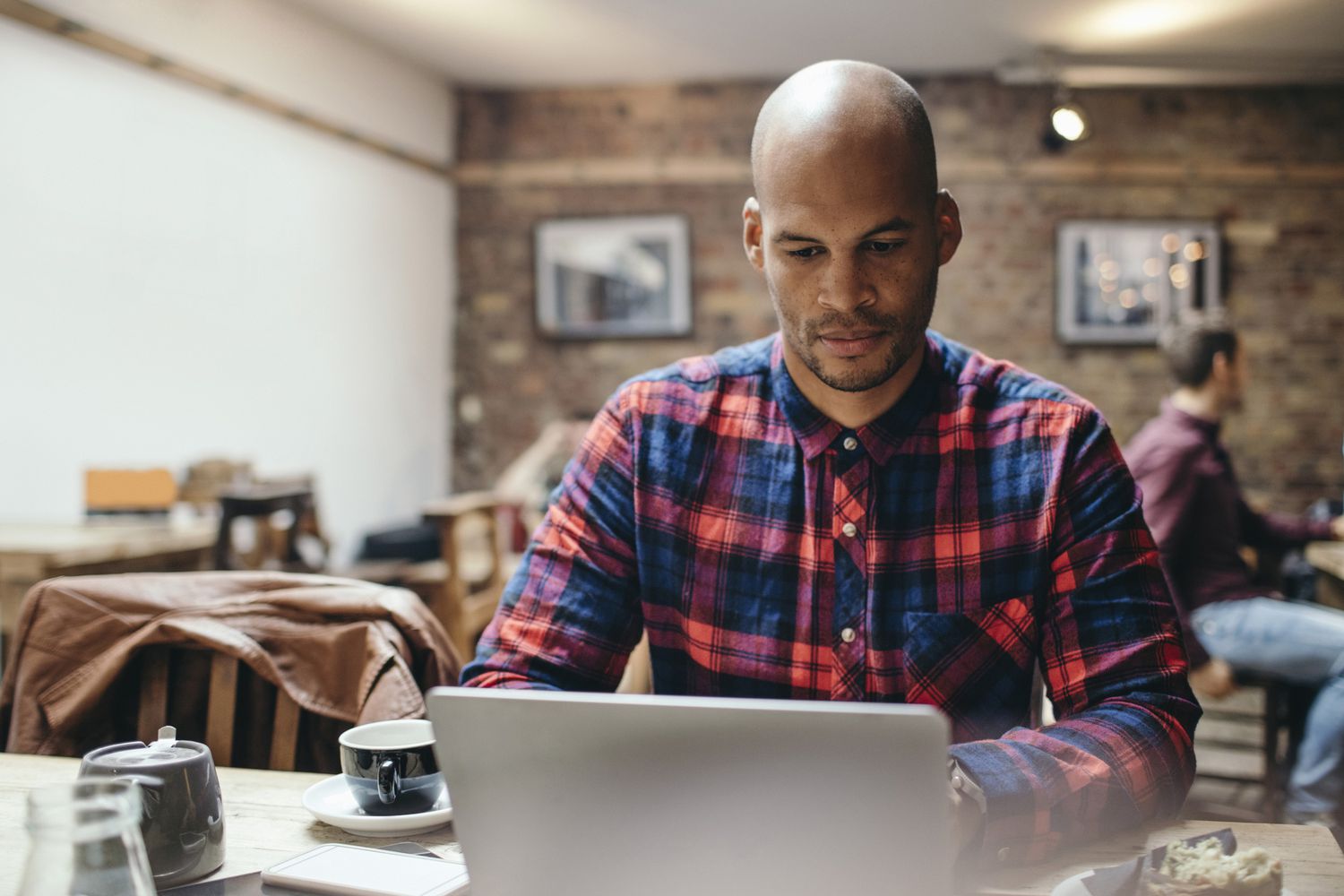 A man in a plaid shirt looks at his laptop in a coffee shop