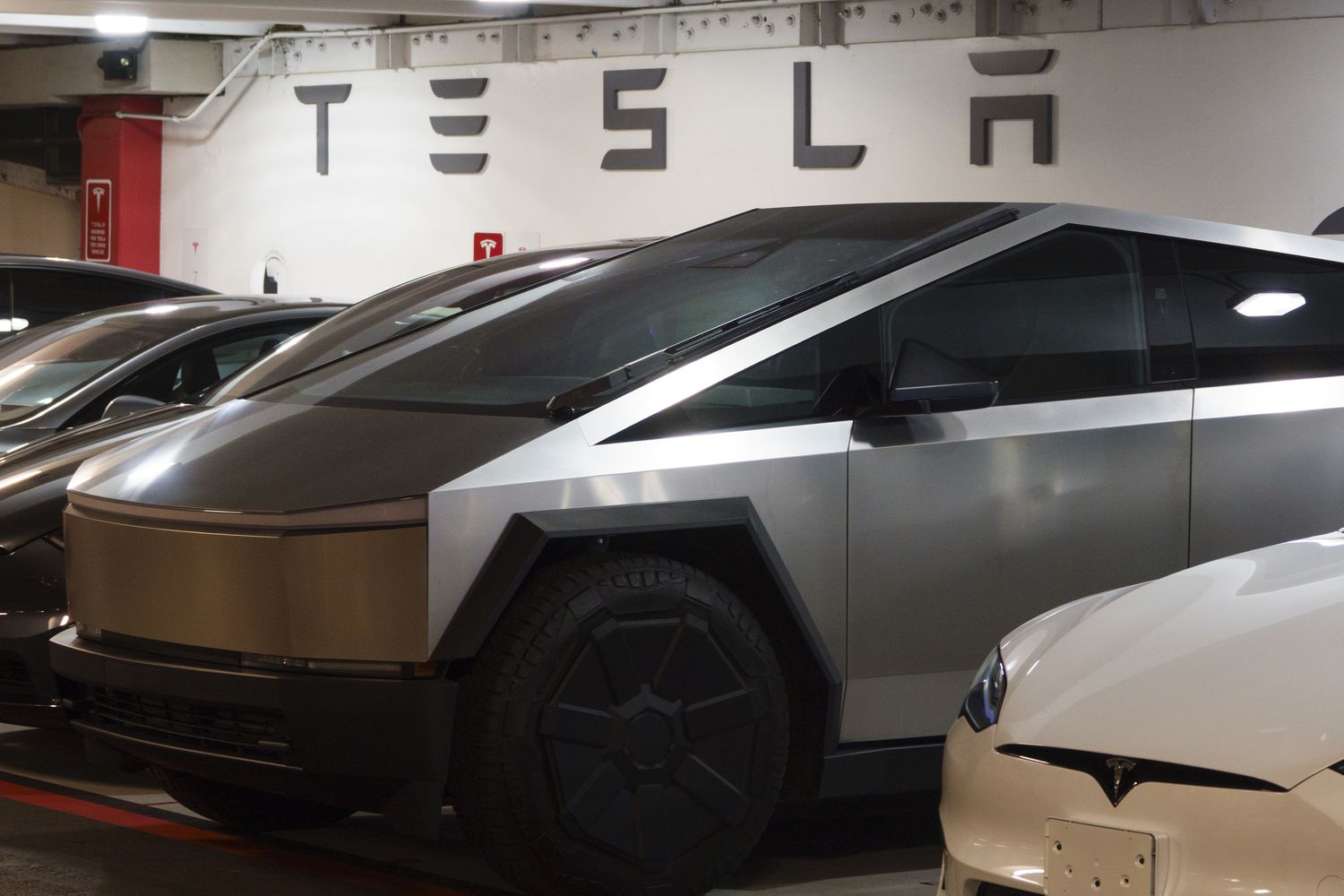 Tesla vehicles are seen in front of a wall with the Tesla logo.