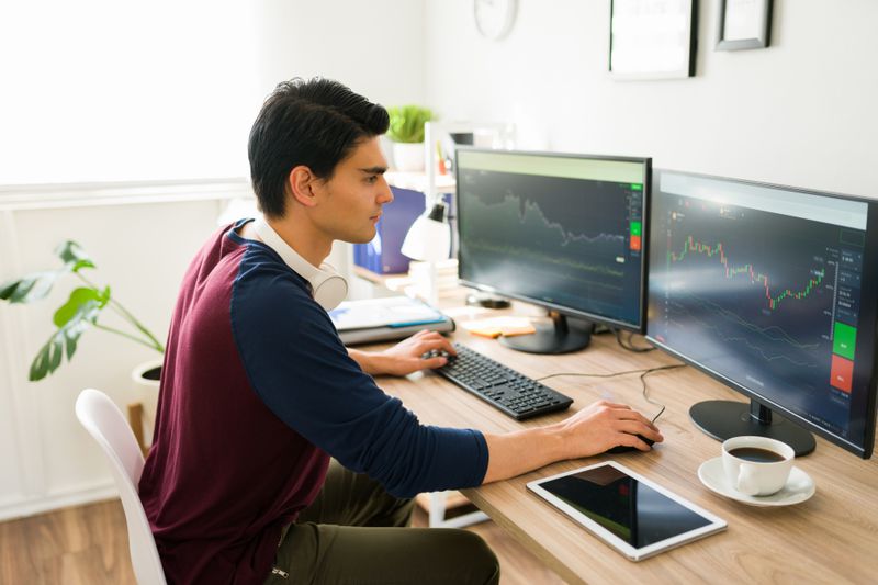A young adult investor uses a home office computer to sell one stock and buy another.