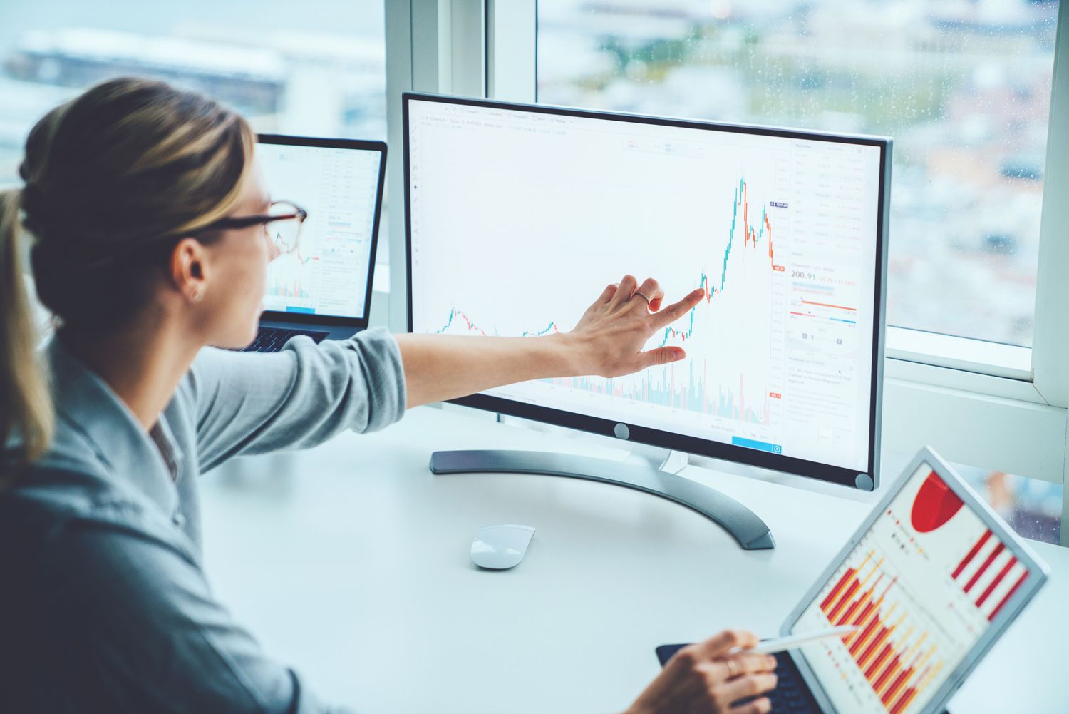 Woman pointing to market data on a computer screen while seated at a desk