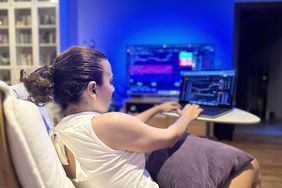 Female trader sitting on a low chair with a cushion on her lap working on a laptop.