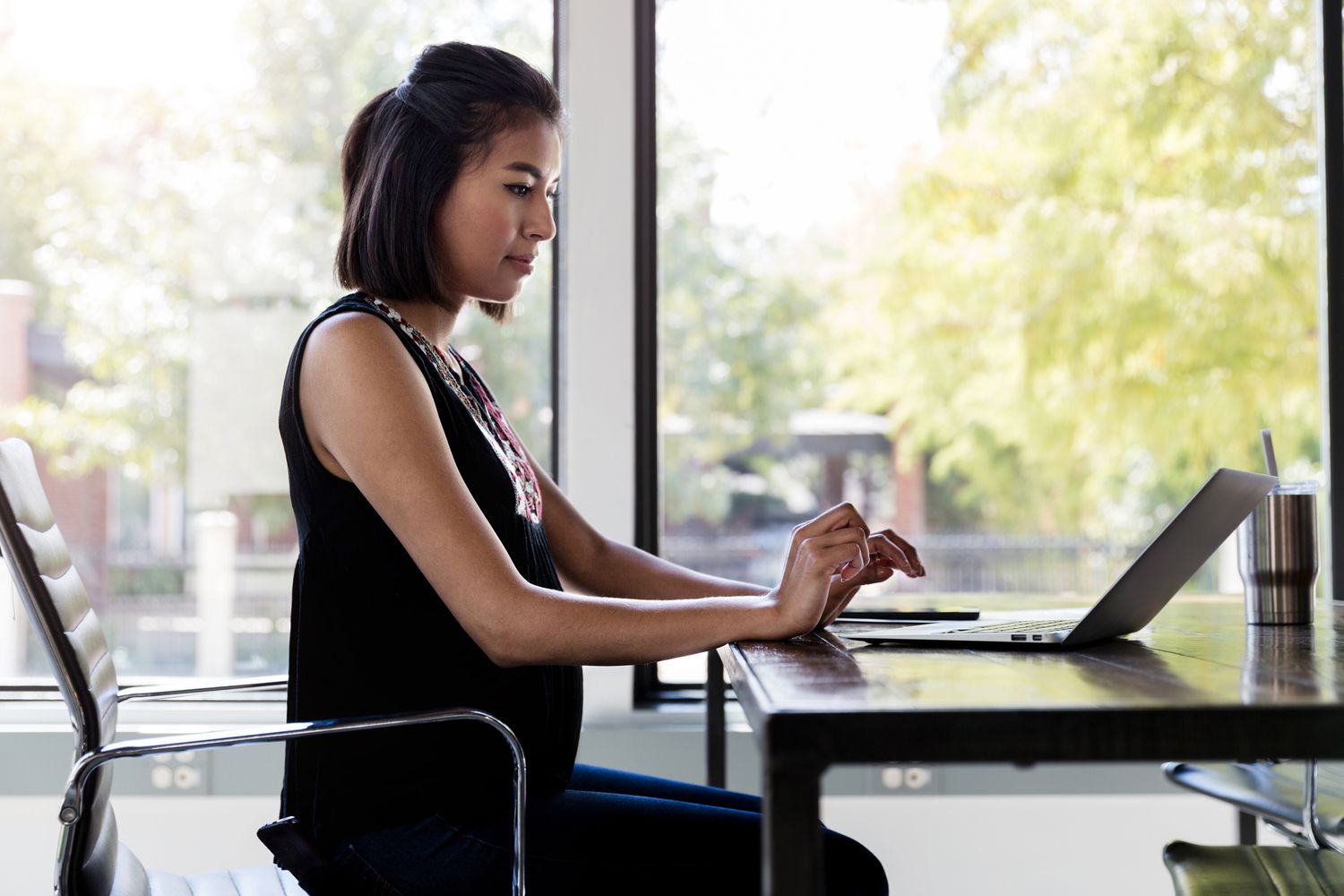 A pregnant woman works on a laptop.