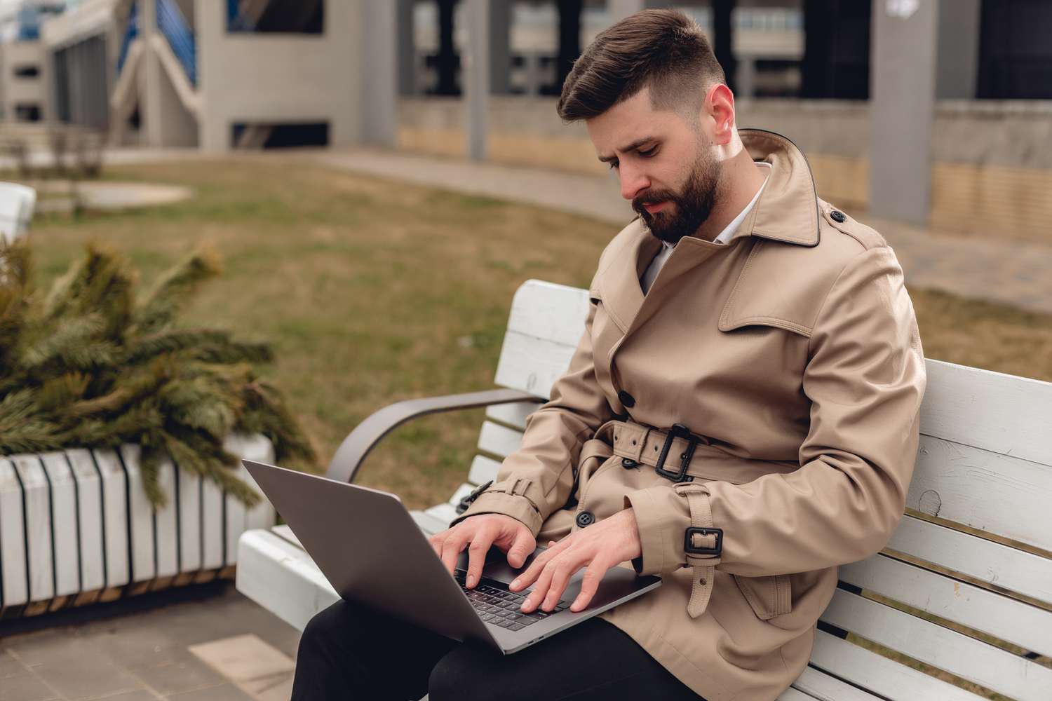 Bearded man sitting on a park bench while working on a laptop