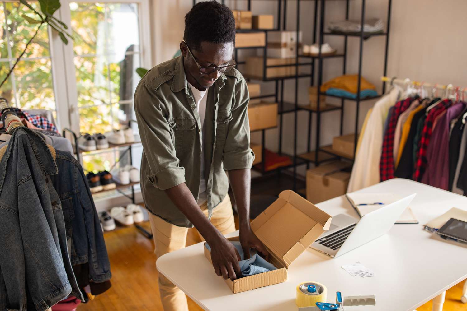 A small business owner prepares a package for shipping, folding a shirt into a box.