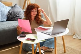 Young adult sitting on the floor at home, feeling stressed while checking on personal finances at home and trying to figure out a way to fix credit with no money.