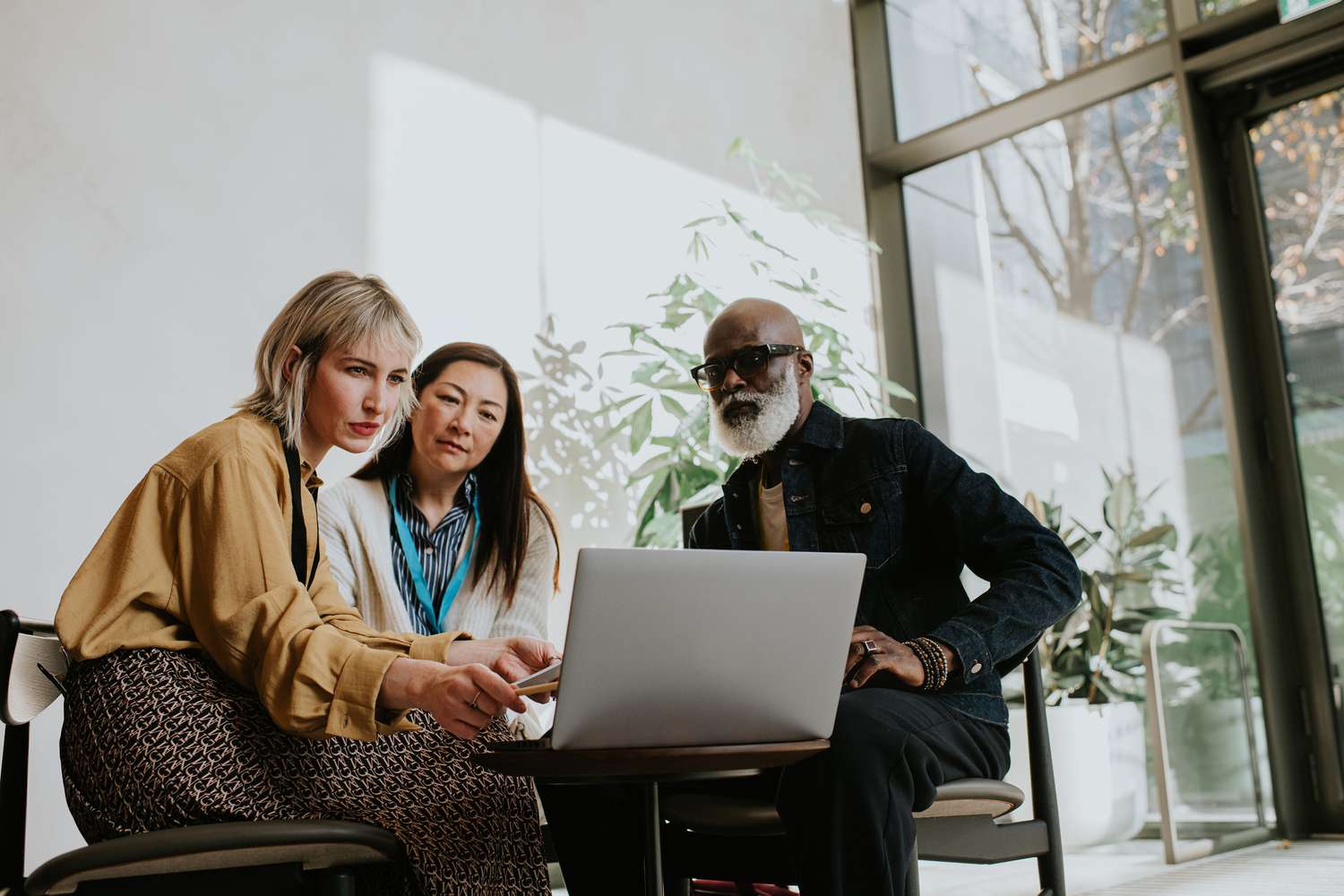 Three people sit around a laptop. One woman is presenting to the group