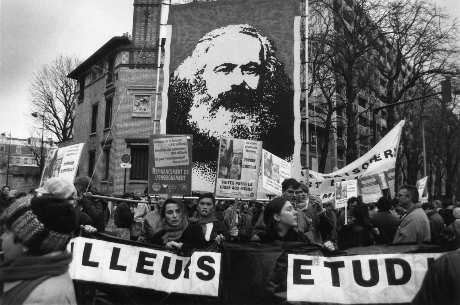 French workers strike for better wages in 1990 and carry a banner with an image of Karl Marx, showing the lasting importance of his ideas and activism. Learn about Marxist sociology here.