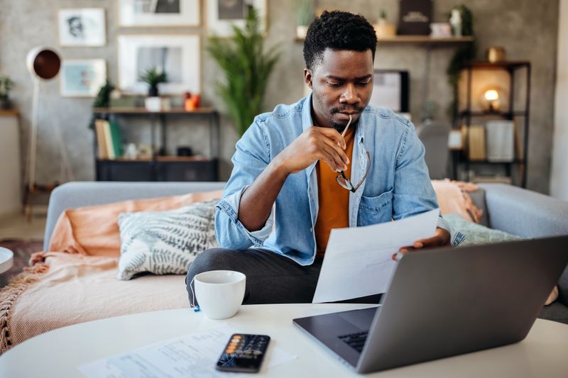 A young man looking over his finances, holding glasses.