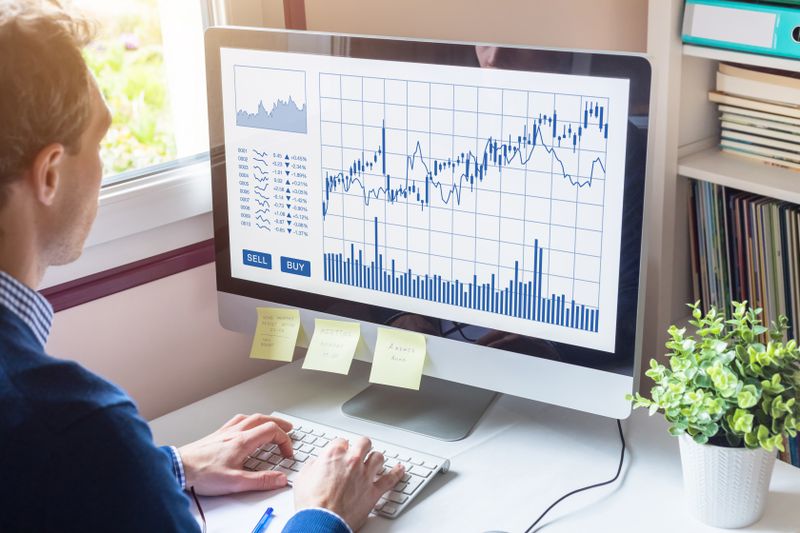 Man at desk looking at candlestick chart on monitor