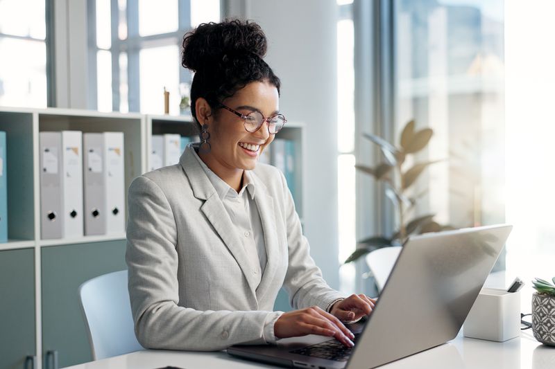 Woman typing on a laptop in an office setting with open and airy windows.
