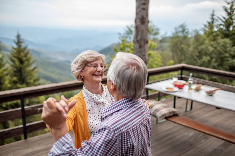 Senior couple slow dancing on a wooden deck with forests in the background.