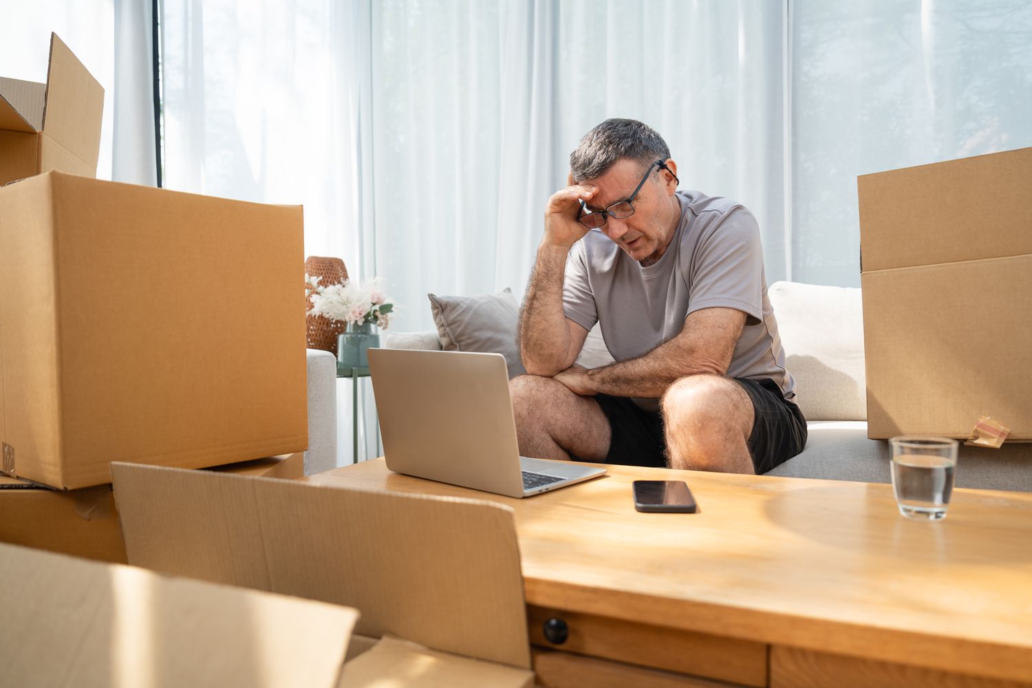 A despondent homeowner sits surrounded by cardboard boxes after filing bankruptcy and being forced to sell their home.