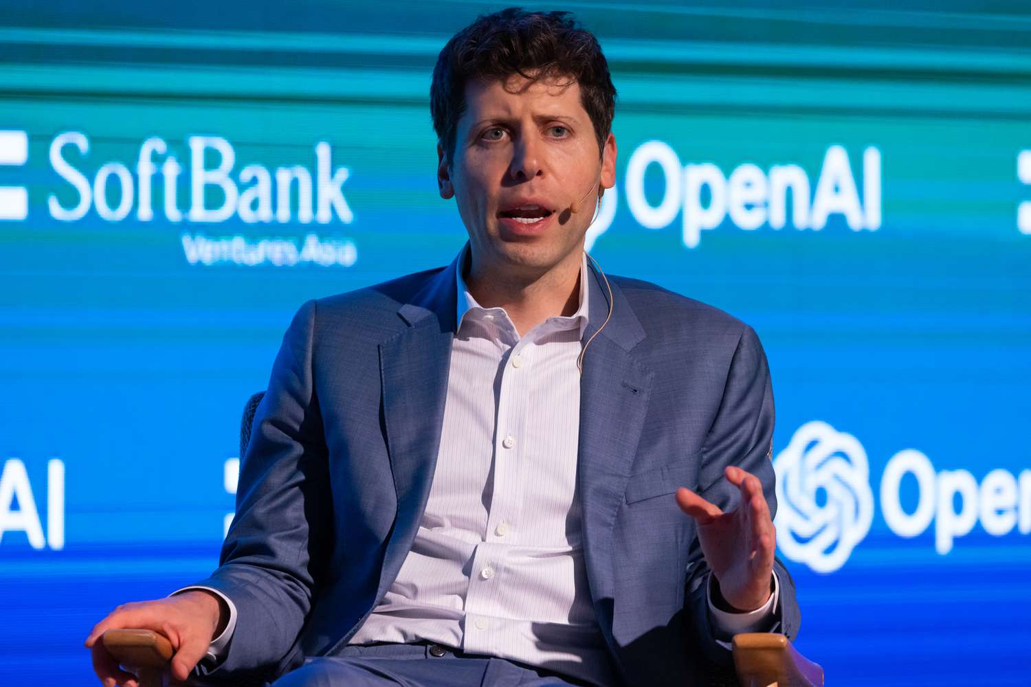 Sam Altman CEO of OpenAI, sitting on a podium with OpenAI sign behind him