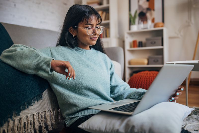 Leisurely reclined, a woman with stylish glasses uses a laptop in the comfort of her contemporary living area