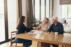 An elder law attorney shakes hands with her clients, a mature couple seated at a long table.
