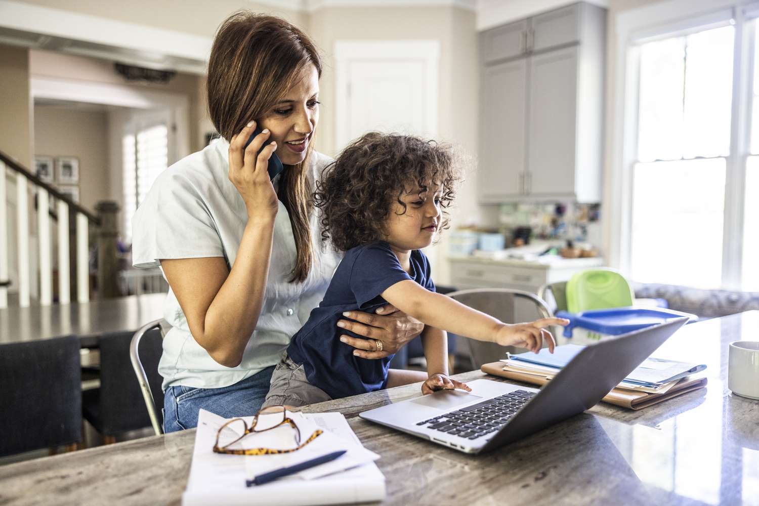 Woman on the phone working from home with her toddler on her lap.