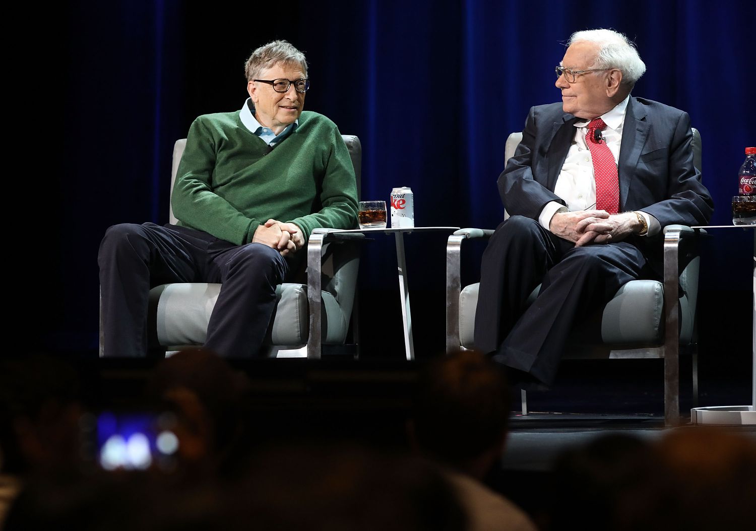Bill Gates and Warren Buffett sit beside each other on stage, speaking at a Columbia Business School event. 
