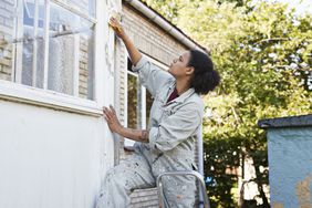 Woman sanding trim on the outside of a house during a home renovation
