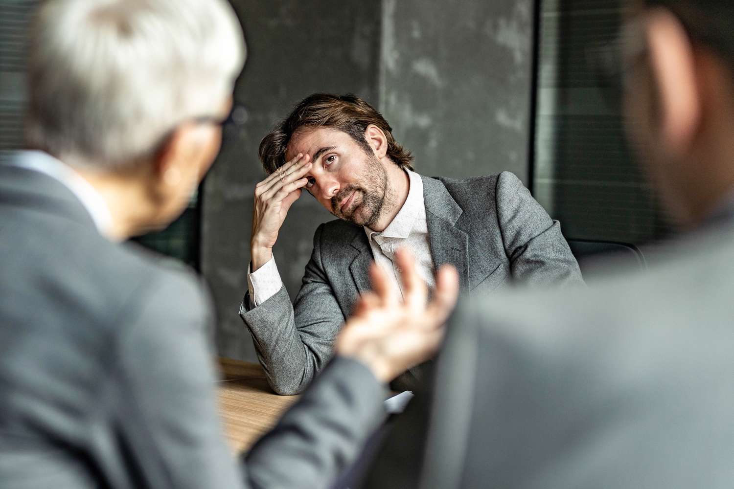 A member of a business management team holds their forehead and looks upset after learning the company is being acquired.