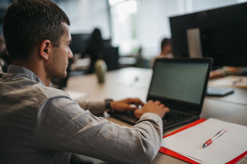 Young serious businessman sitting at desk and working on laptop in modern office