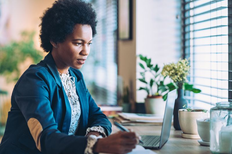 Woman holding a pen and looking at a laptop