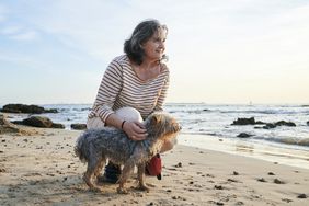 A woman on the beach pets a dog.