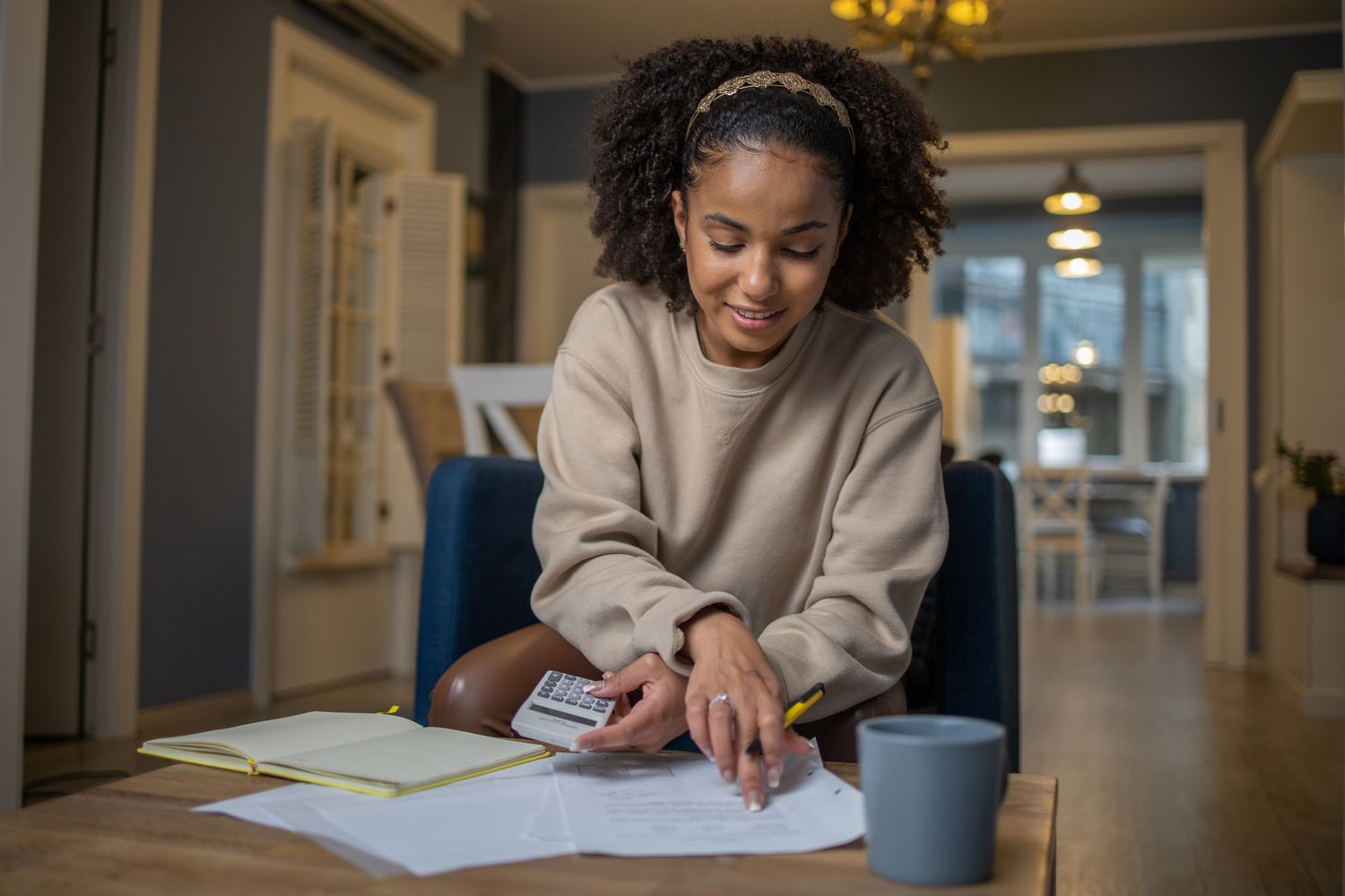 A young woman holding a calculator and a pencil looking at documents on a table.