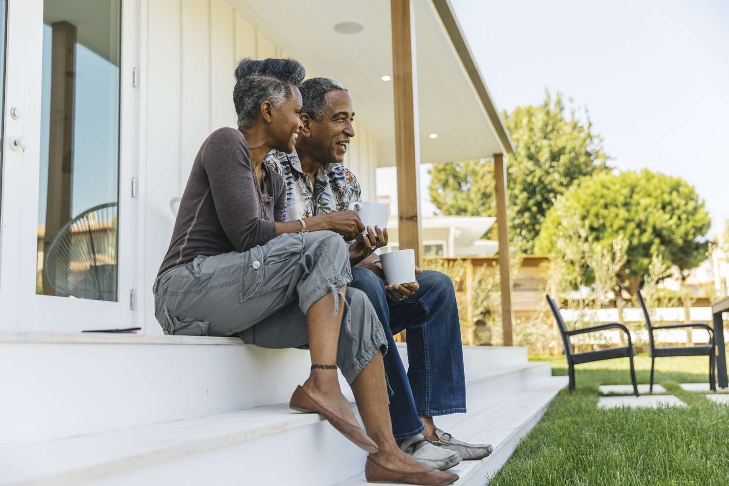 A man and a woman sip coffee while sitting on steps of front porch of house