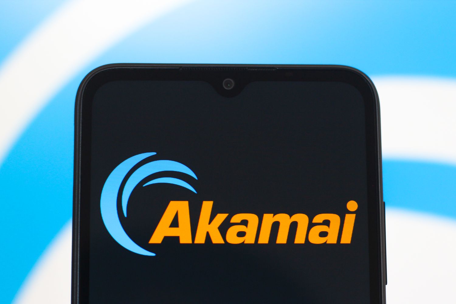 Orange and blue Akamai Technologies logo on a phone screen, in front of a white and blue background