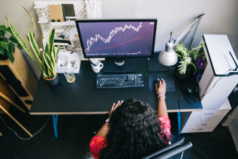 Overhead view of a woman sitting at a desk studying charts on a computer.