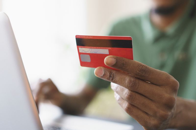 A hand holding a credit card over a laptop