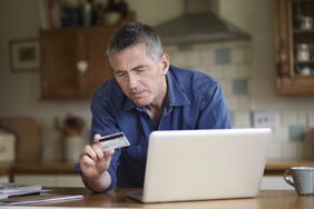 Man holding credit card using laptop in kitchen