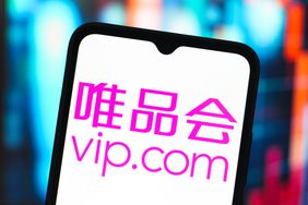 The pink Vipshop Holdings logo is seen on a phone screen in front of a blue and orange background.