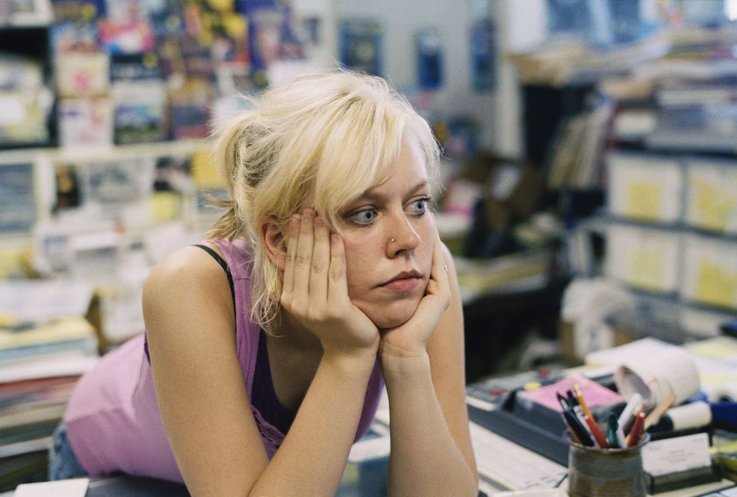 A small business owner leans on the service counter in their store while they wait for business to pick up.