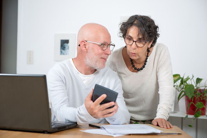 Older couple sitting at home and looking at mortgage documents, a calculator, and a laptop