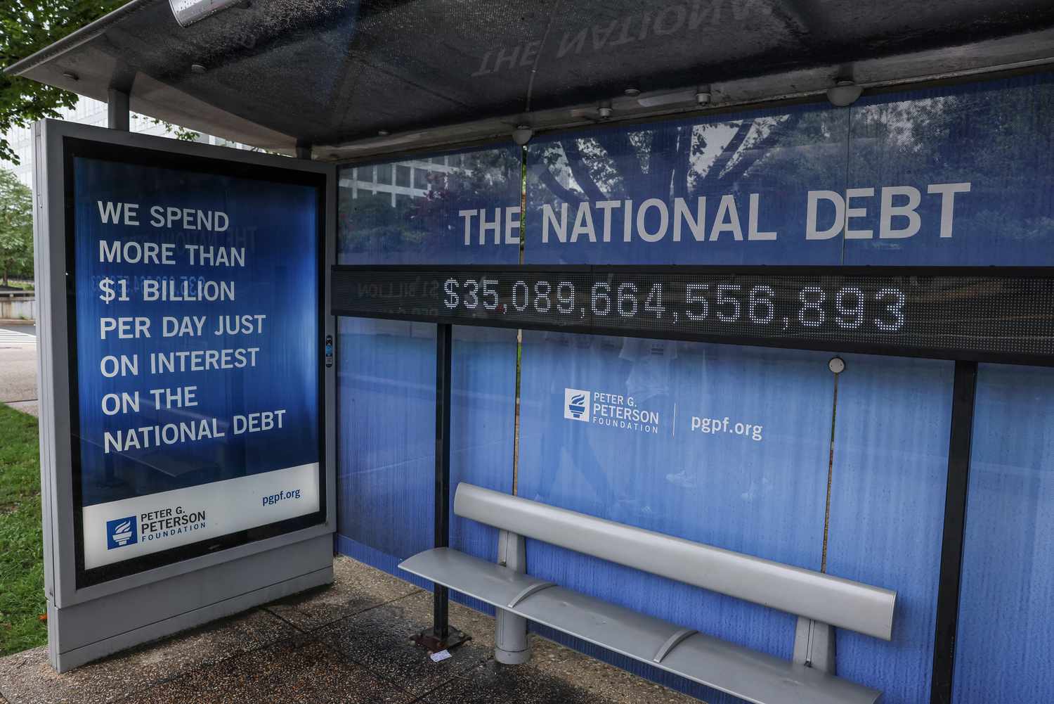 A view of a bus shelter at Independence Avenue and 9th St's SW where an electronic billboard and a poster display the current U.S. National debt 