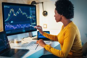 Woman with a laptop, tablet, and large monitor showing stock charts