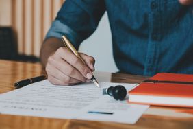 Close up of customer signing contract with fancy, heavy pen while sitting at desk