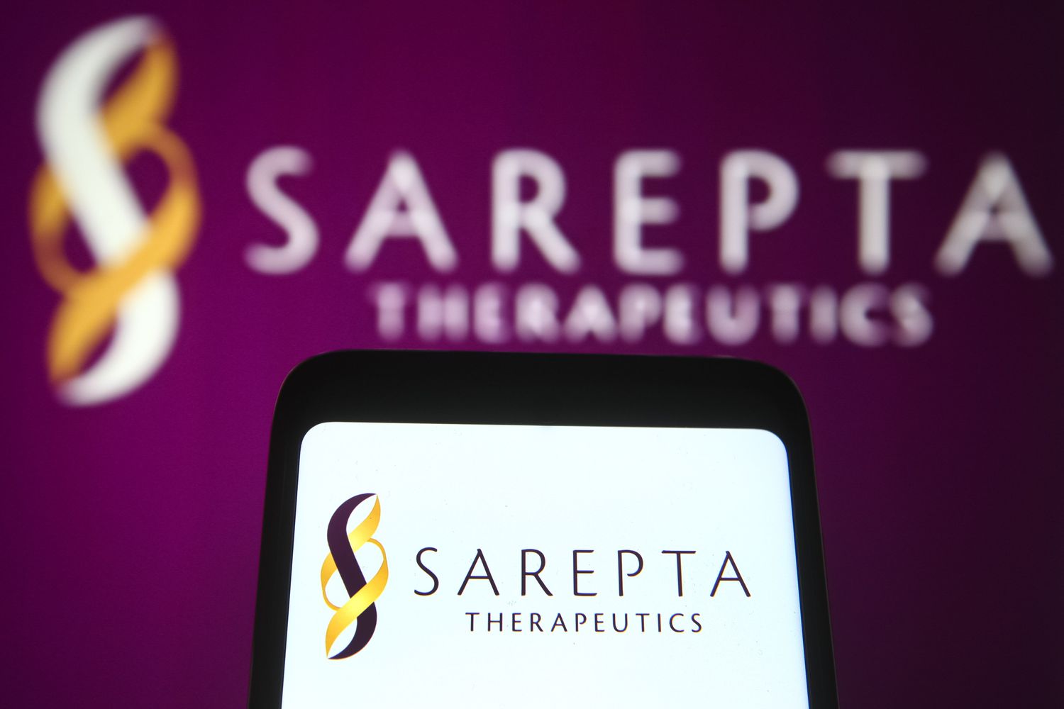 A Sarepta Therapeutics logo is seen on a smartphone and a PC screen