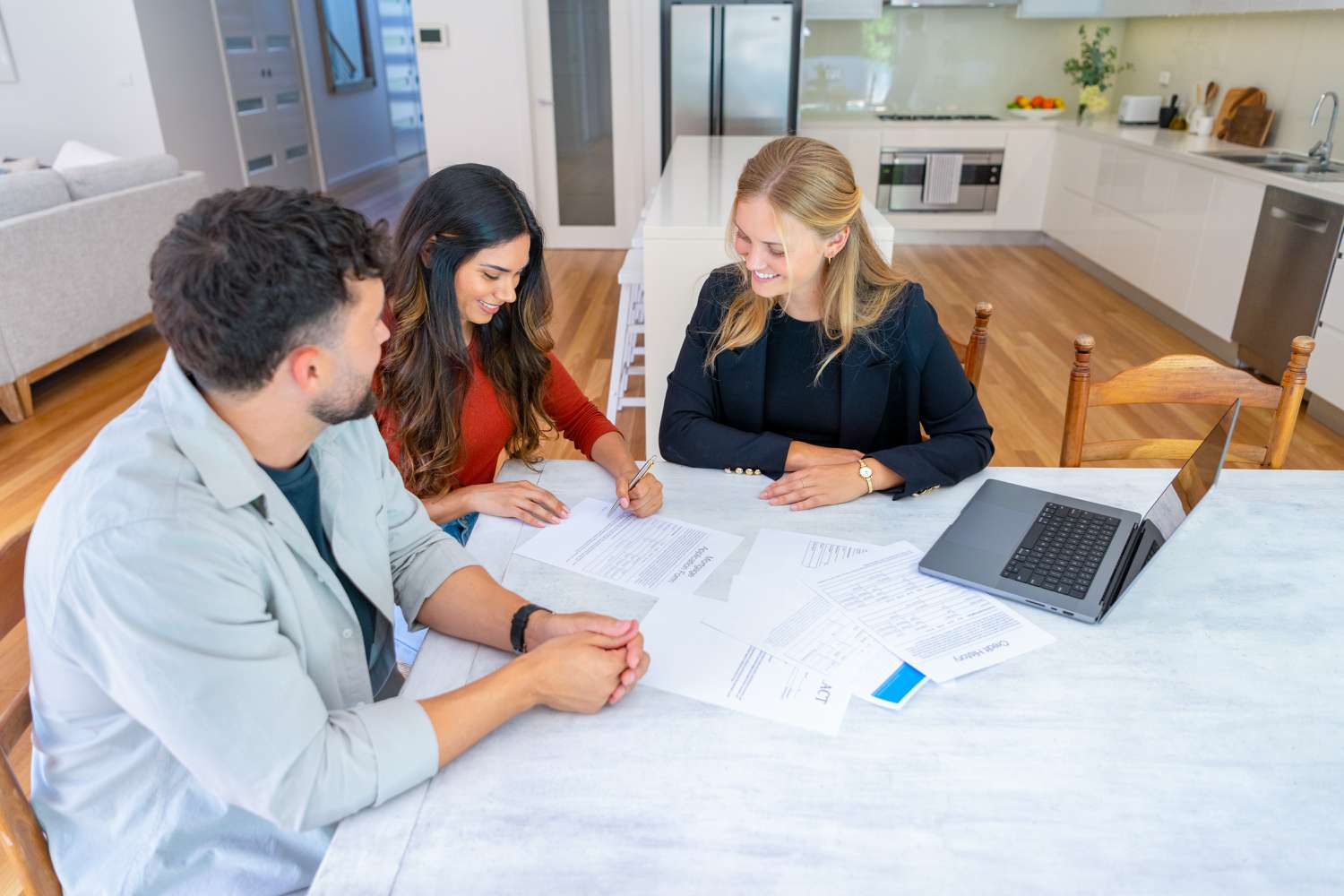 A man and a woman sit at a table with another woman signing papers