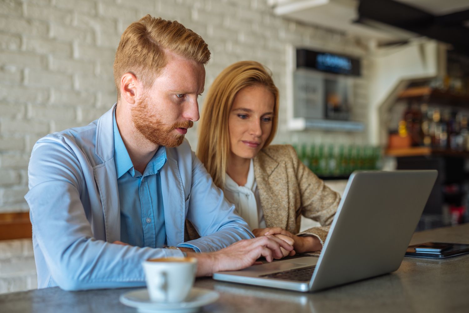 Couple in their 20s or 30s sitting in a coffee shop and looking at online mortgage rates