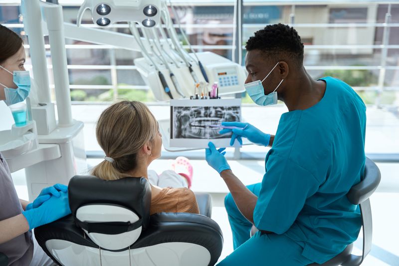 Dentist pointing out details on a mouth x-ray to a patient sitting in a dental chair