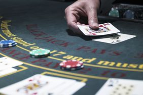 Male croupier holding card at Blackjack table.