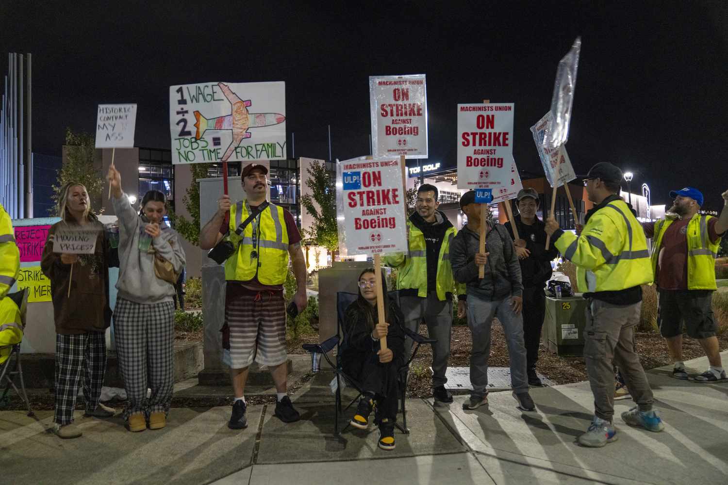 A group of workers hold picket signs that have various messages about being on strike against Boeing