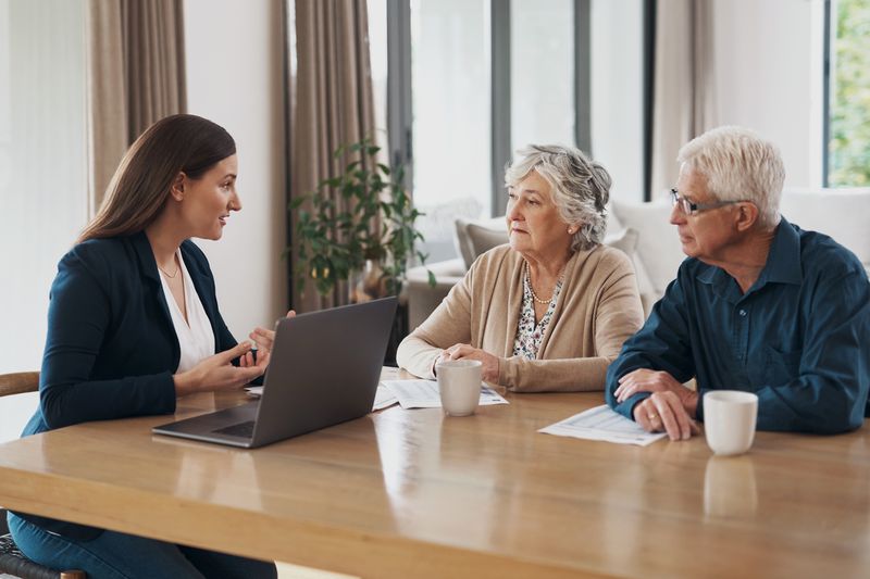 A woman conversing with an elderly couple at a table with a laptop