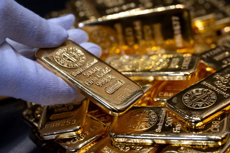 A gloved hand holding a gold bar among several others