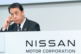 Nissan CEO Makoto Uchida sits at a microphone at a white podium during a press conference.